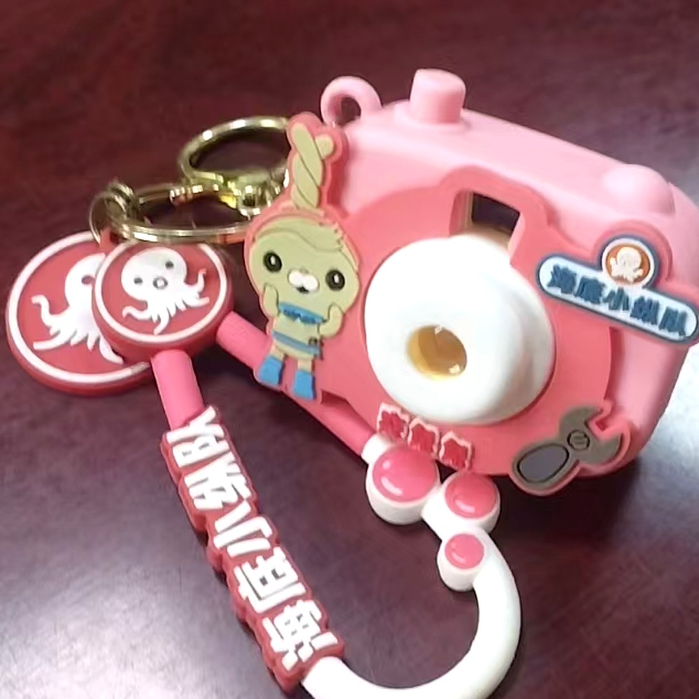 Custom multi-part soft casing set: a camera-shaped moulded keyring supplied with a sculpted character charm, two round moulded badges and a raised-letter strap